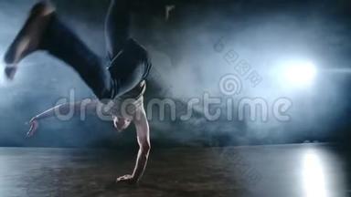 现代芭蕾，一个人从舞台上的一个坐姿，在烟雾中的一个黑暗的舞台上，旋转着跳回