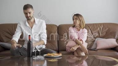 英俊的男人用开瓶器打开酒瓶，而他的妻子坐在附近。 幸福的夫妻浪漫的晚餐