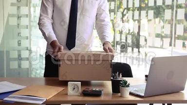 辞职后，年轻的男员工站在工作桌旁，把他的东西放进纸箱里