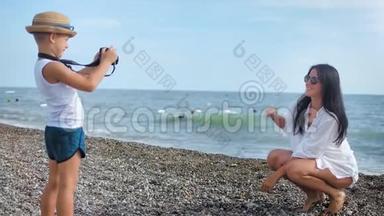 在男孩用相机拍照时，在海滩上摆姿势拍照的免费旅游妇女