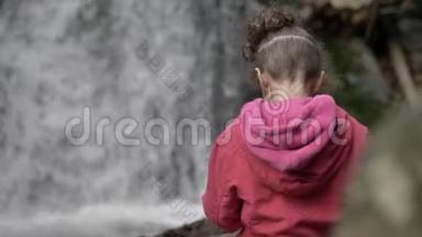 可爱可爱的小女孩，有着有趣的发型，在野外观看美丽的瀑布