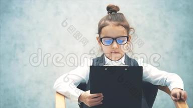 一个女学生`<strong>商务</strong>女孩仔细阅读一个黑色文件夹。 坐着的女孩是<strong>灰</strong>色<strong>背景</strong>。 戴眼镜严重