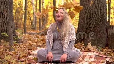 一位孕妇正坐在秋林中的一棵树下。 黄色的叶子在飘落。 慢动作