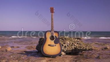 在海滩或海岸或海洋上的西方吉他。 吉他独自靠岸，海浪在石头上，岩石上。