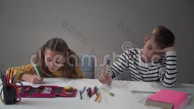 一个男孩在桌子上扔钢笔的肖像。 他那勤奋的妹妹惊讶地看着他，继续写着