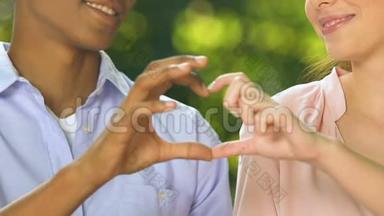 幸福的多种族情人一对秀心用手指歌唱爱与关怀，约会