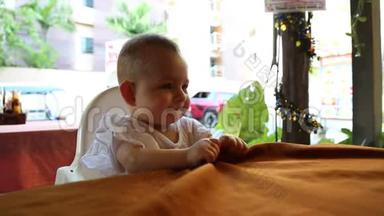 一个快乐的一岁小女孩正坐在一个<strong>特殊儿童</strong>座位上的咖啡馆里的桌子旁。
