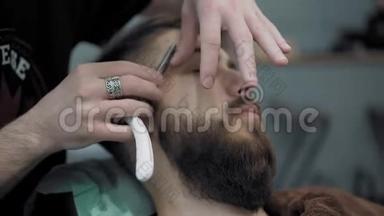 理发师在理发店或理发店用直刃剃须刀刮胡子。 男人`理发和刮胡子