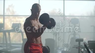 一位运动员在一扇有着美丽身体的窗户的背景下，举重来训练你在健身房里的二头肌。 <strong>实力</strong>