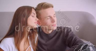 一对年轻可爱的白种人夫妇深情地拥抱着，看着坐在一起的摄像机特写照片
