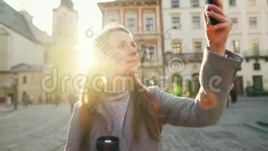年轻的微笑女子穿着灰色外套，手里拿着一个保温杯，在漂亮的建筑智能手机上拍照