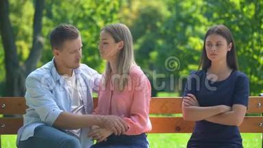 恋爱中的情侣坐在长凳上拥抱和聊天，无视他们的朋友