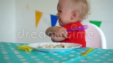 心烦意乱的蹒跚学步的孩子男孩坐在桌子旁吃饺子。 万向节运动