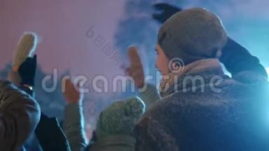 年轻人在城市广场的圣诞音乐会上聚会。 朋友们用挥动的双手跳起来，用手跳舞