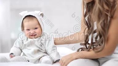 微笑的婴儿穿着可爱的整体坐在床上，有积极的情绪看着相机