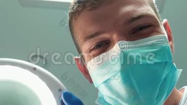 年轻英俊的微笑<strong>医生</strong>，<strong>戴口罩</strong>的牙医手持医疗灯，在病人`检查时使用牙科镜
