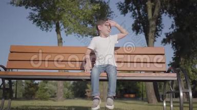 可爱的小男孩坐在公园的长凳上。 可爱的孩子独自呆在户外。 夏日休闲
