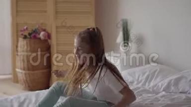有趣可爱的小女孩带着耳机在床上听音乐。 年轻的音乐爱好者在家玩音乐