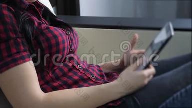 网上购物的概念。 坐在网上商店看商品的年轻女孩在数码平板电脑上购买。 妇女