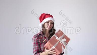 快乐美丽的女人戴着圣诞帽和睡衣摇动礼盒。 假日概念。 慢动作