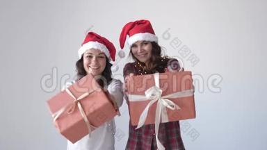 穿着圣诞帽和睡衣的年轻漂亮女人在白色背景上送礼物盒。 女人手里的小礼物。