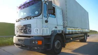 摄像机跟随卡车与货物拖车在公路上行驶和运输货物。 卡车在农村超速行驶