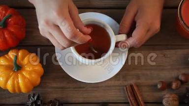 妇女手拿茶匙，在木桌上搅拌热茶，背景是南瓜、树叶、香料。秋季<strong>大会</strong>