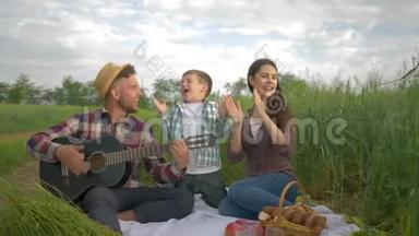 快乐的家庭，快乐的爸爸弹吉他，妈妈带着儿子唱歌拍手，在绿色的田野里放松地野餐