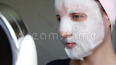 女人正在使用泡泡面膜来护肤。 女人在看化妆镜。