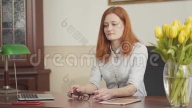 可爱的红发女心理学家坐在桌子旁，在办公室等病人。 心理健康。
