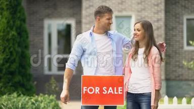有吸引力的夫妇拥抱在房子前面安装销售招牌，生活