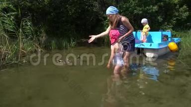 带着孩子在湖岸喂鸭子的女人。 带双体船的刺激旅行