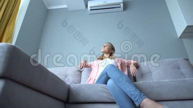 年轻女子坐在空调下的沙发上，在炎热的夏天降温