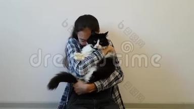 一个穿格子衬衫的女孩拥抱她最喜欢的黑白猫。 胖乎乎的小猫对这样的温柔不太满意。 有趣的动物