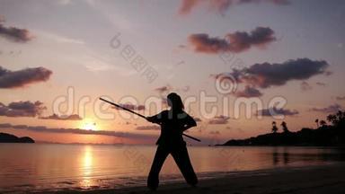 一位年轻有权势的女人用一根<strong>功夫</strong>棍子站在海滩上的剪影