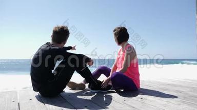 年轻的男人和女人坐在岩石海滩上。 男朋友指指<strong>点点</strong>指海天，说话.. 慢动作