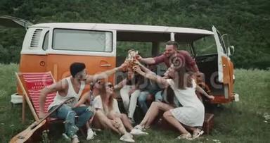 一大群朋友在野餐聚会上喝着啤酒和<strong>欢呼声</strong>，坐在一辆复古面包车后面