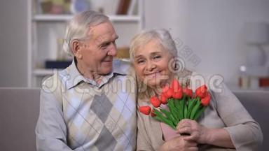 一对老夫妇在家拥抱，一个女人拿着一束郁金香，结婚纪念日礼物