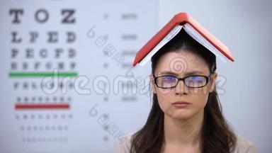 女士头上拿着书看着摄像机，过度劳累的学生准备考试