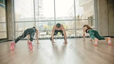 工作室的健身训练-两名妇女和她们的教练靠在地上，向前爬行-站起来，
