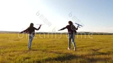 玩具飞机在女孩手中，她们在野外玩耍。 快乐的孩子在草地上，手里拿着一架飞机。 梦想飞翔