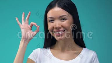 微笑的亚洲女人显示OK手势孤立在蓝色背景，确认