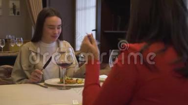 两个漂亮的女朋友坐在现代餐厅里，在一起。 女孩在豪华餐厅品尝新菜