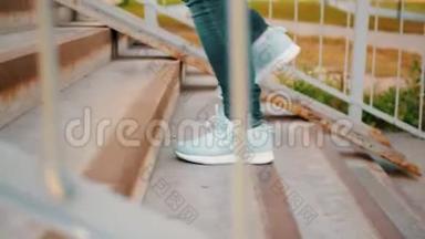 女腿穿着<strong>运动鞋</strong>和蓝色牛仔裤走在楼上室外。 女人的脚在<strong>运动鞋</strong>上爬楼梯