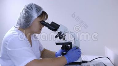 女化验员坐在工作场所做显微镜检查