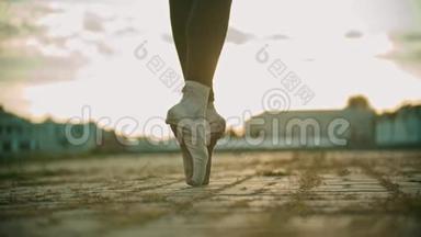 年轻女子芭蕾舞女的腿在她的脚尖上慢慢地走在屋顶上-日落