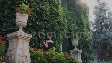 年轻女子在豪华的大花园或宅基地里摆姿势。 她站在绿色的葡萄墙上，抚摸着鲜花