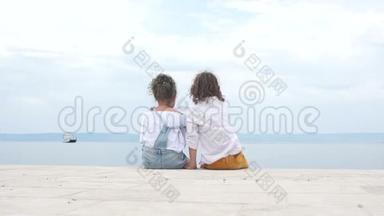 男孩和一个女孩坐在<strong>海边</strong>，看着远处的一艘<strong>帆船</strong>。 旅费