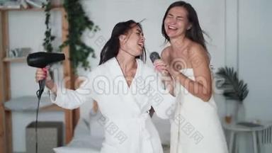 两位年轻女士穿着白色浴袍跳舞，带吹风机唱歌，吹干头发，开怀<strong>大笑</strong>