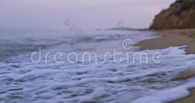 沙滩上的泡沫海浪拍打着沙滩，正被海水拉回，远处有悬崖峭壁